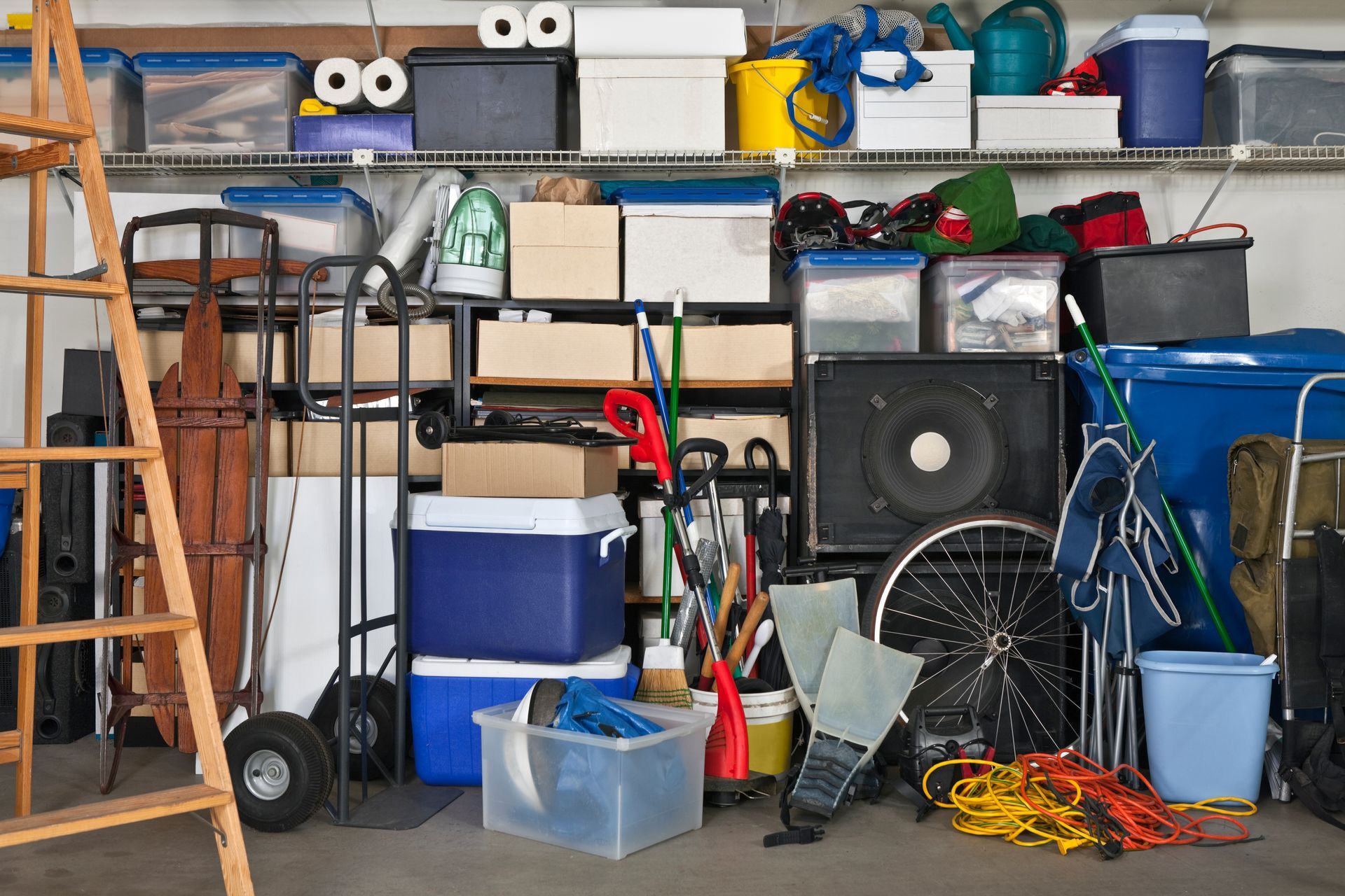 Cluttered garage storage with boxes, tools, and equipment on shelves and floor. Cluttered garage storage with boxes, tools, and equipment on shelves and floor.