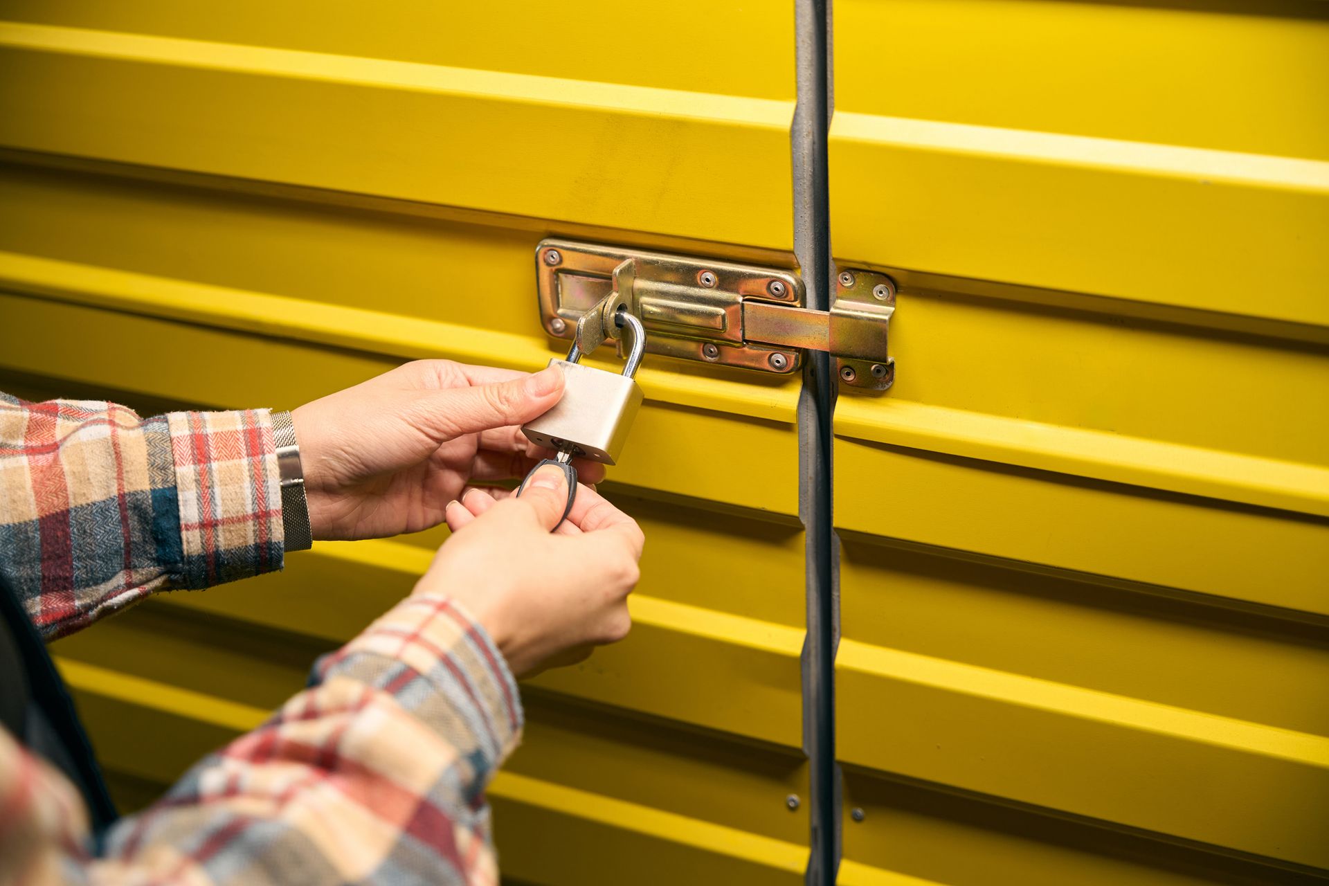 A man's hands padlocking a metal storage unit door.