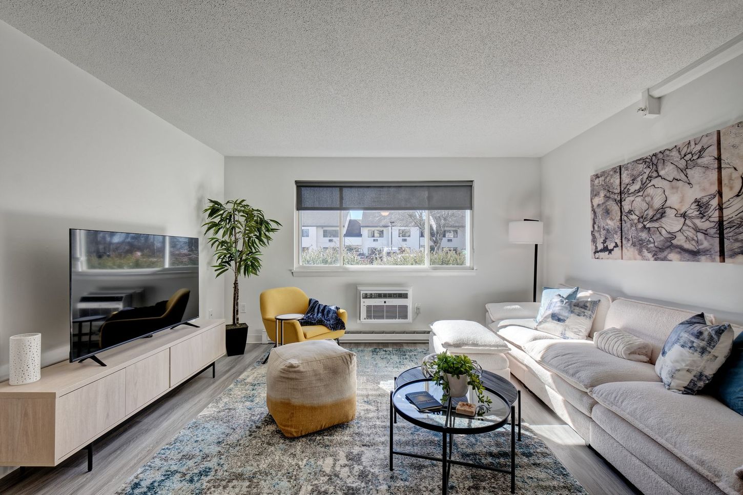 Living room with sofa, TV, armchair, rug, and art on white walls.