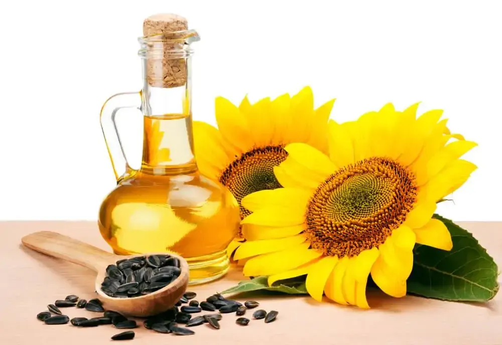 Una bottiglia di olio di girasole accanto a un girasole e semi di girasole.