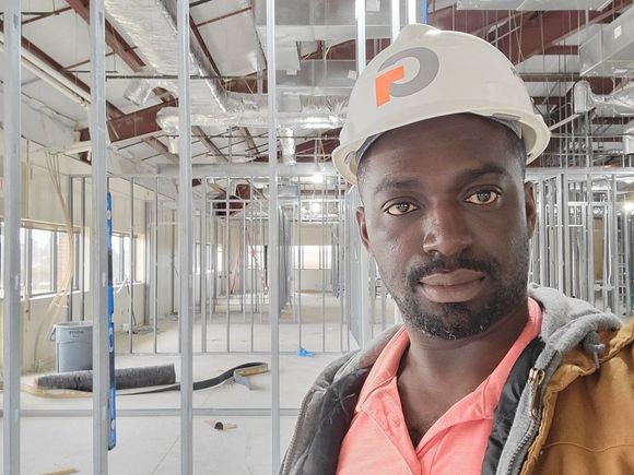 Construction worker in a hard hat, smiles in a building under construction, steel framing visible.