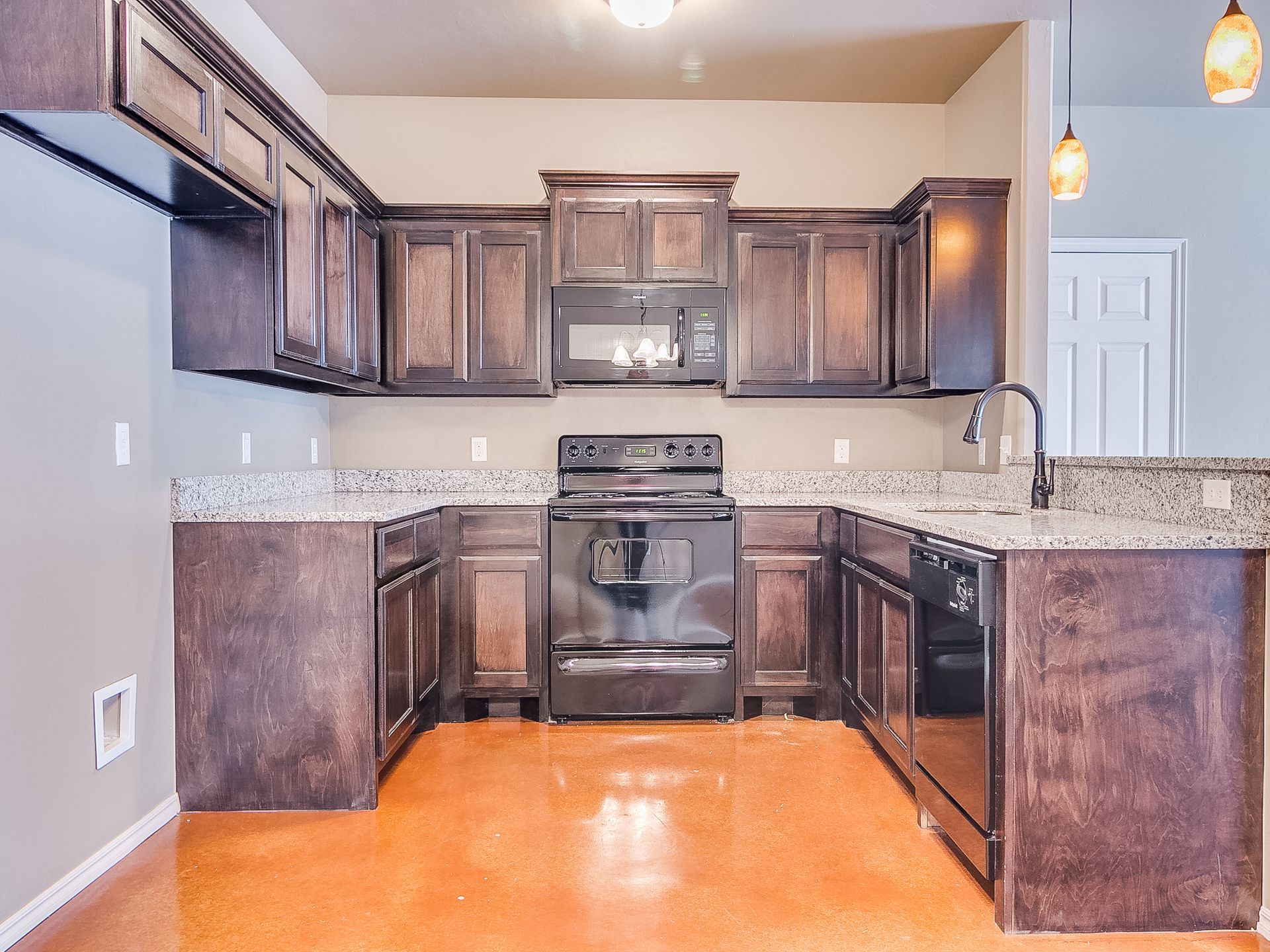 U-shaped kitchen with dark brown cabinets, black appliances, granite countertops, and orange floor.
