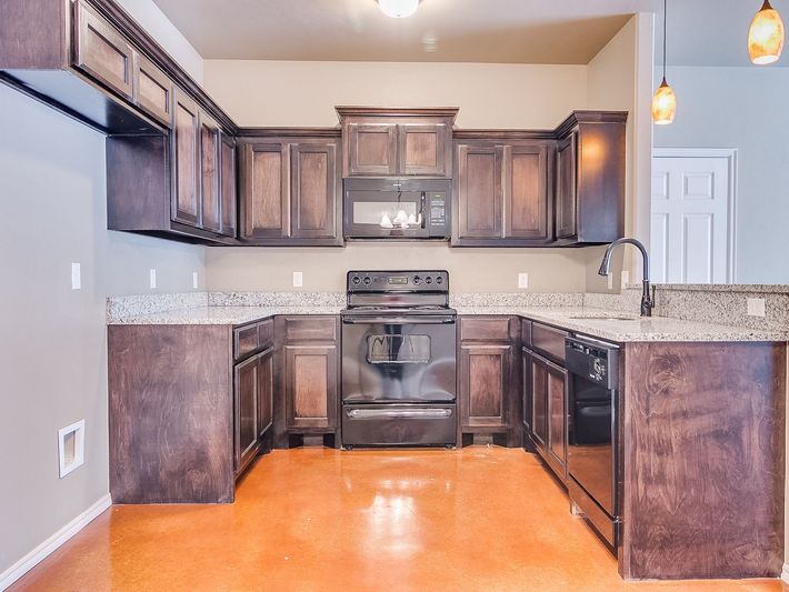 Kitchen with dark cabinets, granite countertops, black appliances, and orange-toned flooring.
