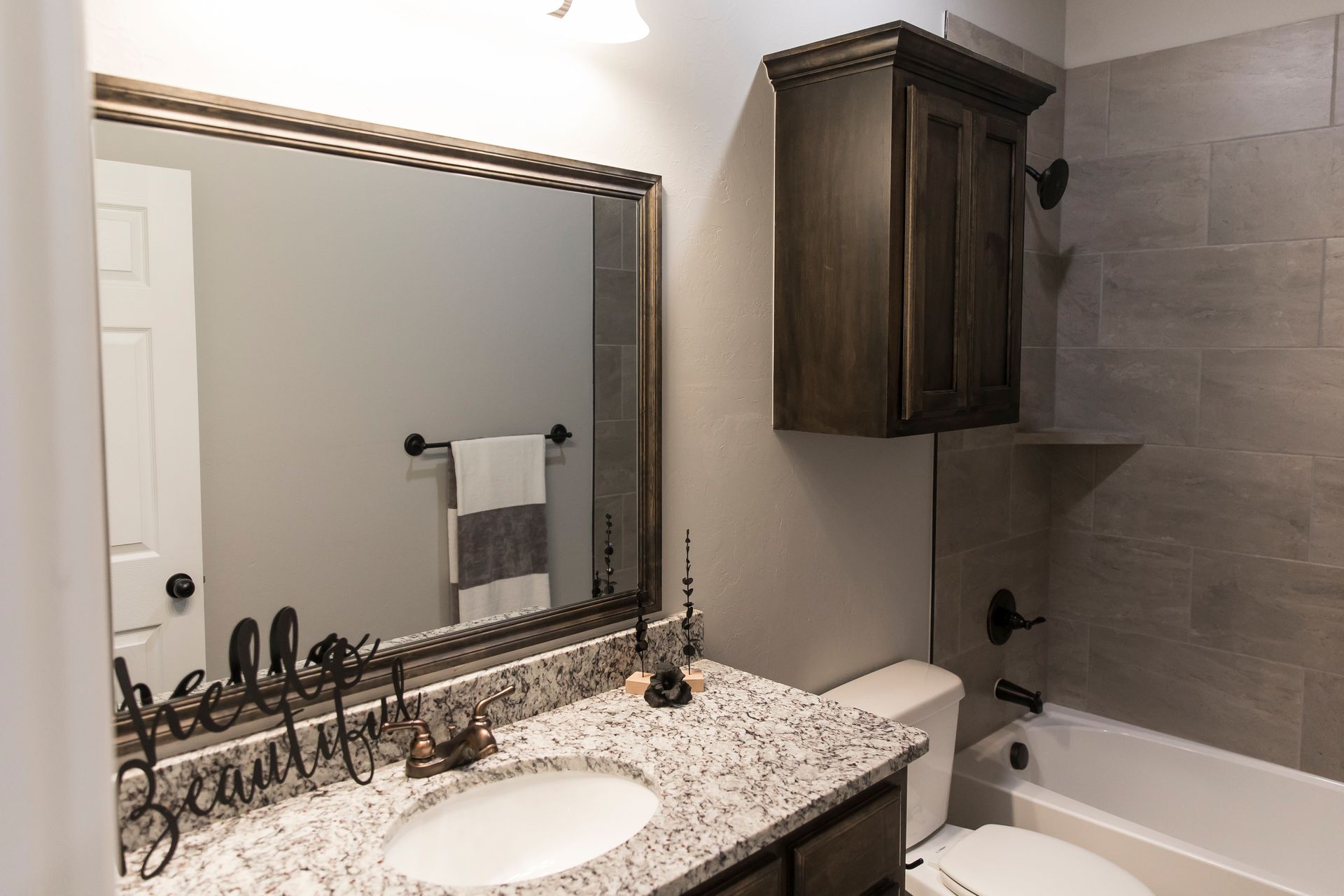 Bathroom with granite countertop, mirror, dark cabinets, and gray tile.
