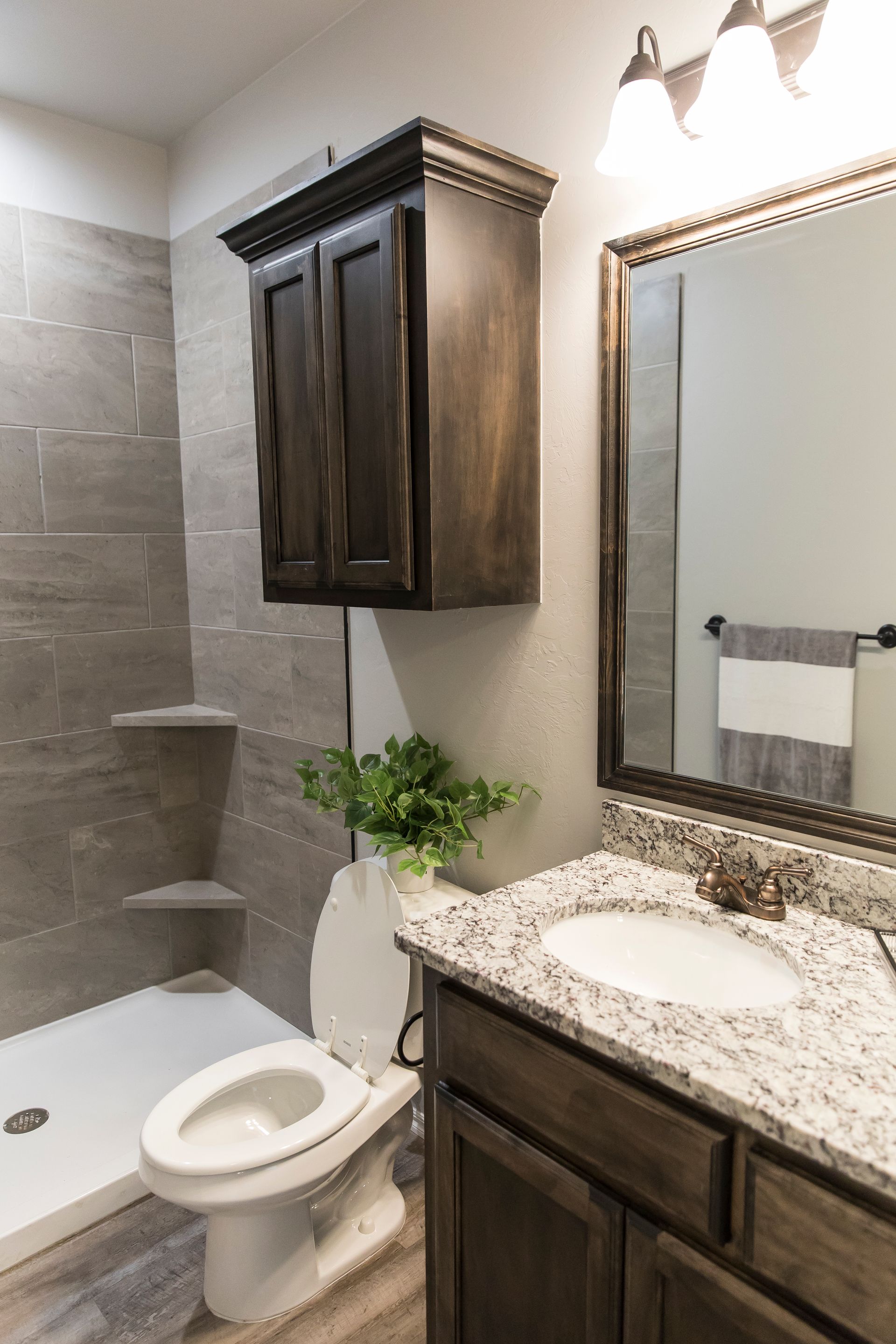 Bathroom with gray tile shower, toilet, dark wood vanity and cabinet, granite countertop, and mirror.