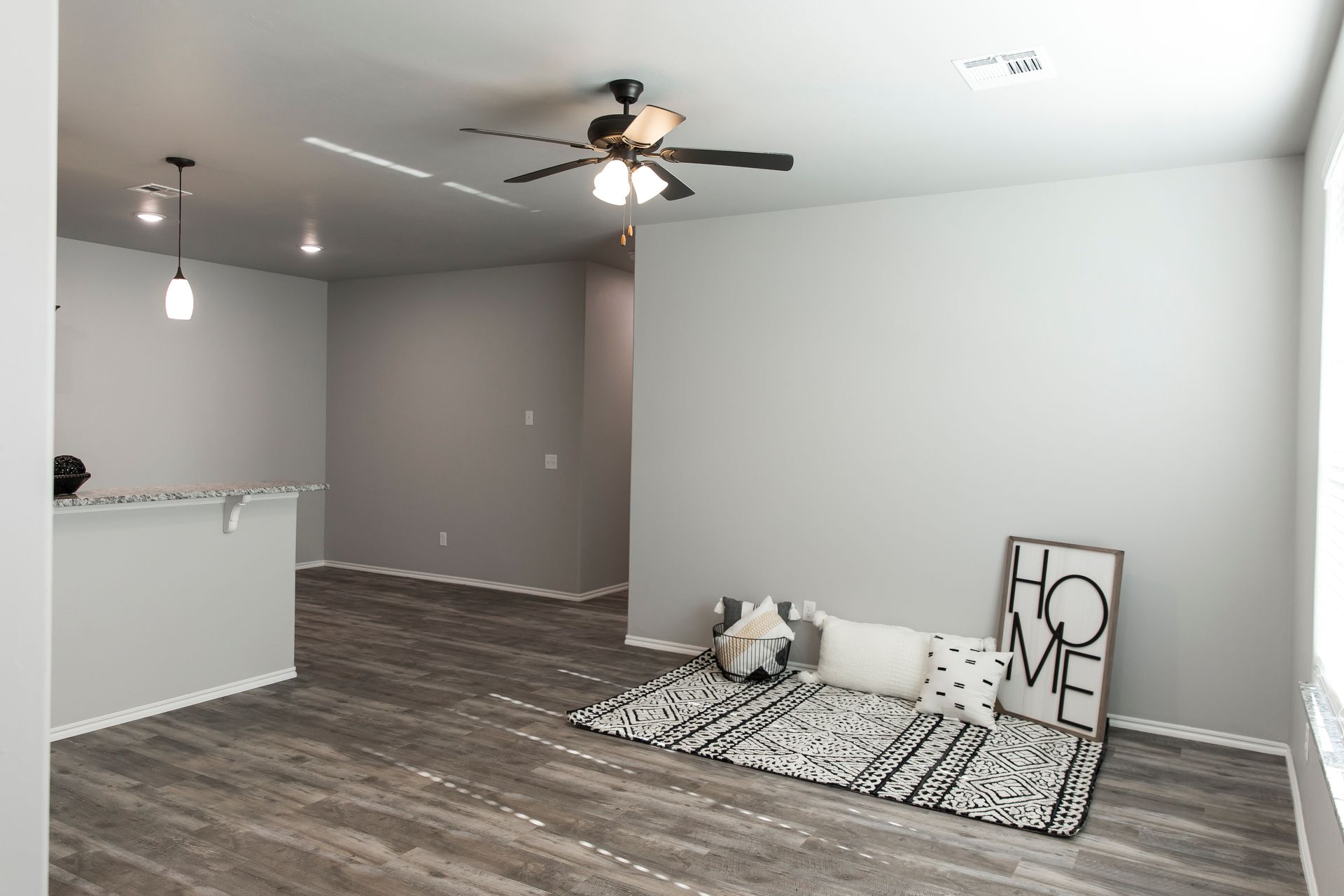 Empty living room with gray walls, wood-look floors, ceiling fan, and