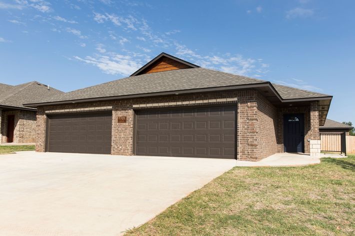 Brick house with brown garage doors and driveway. Blue sky background.