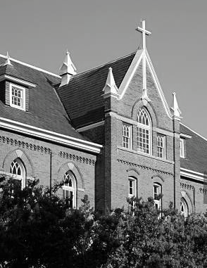 Brick building with cross on a gable, arched windows, and trees.