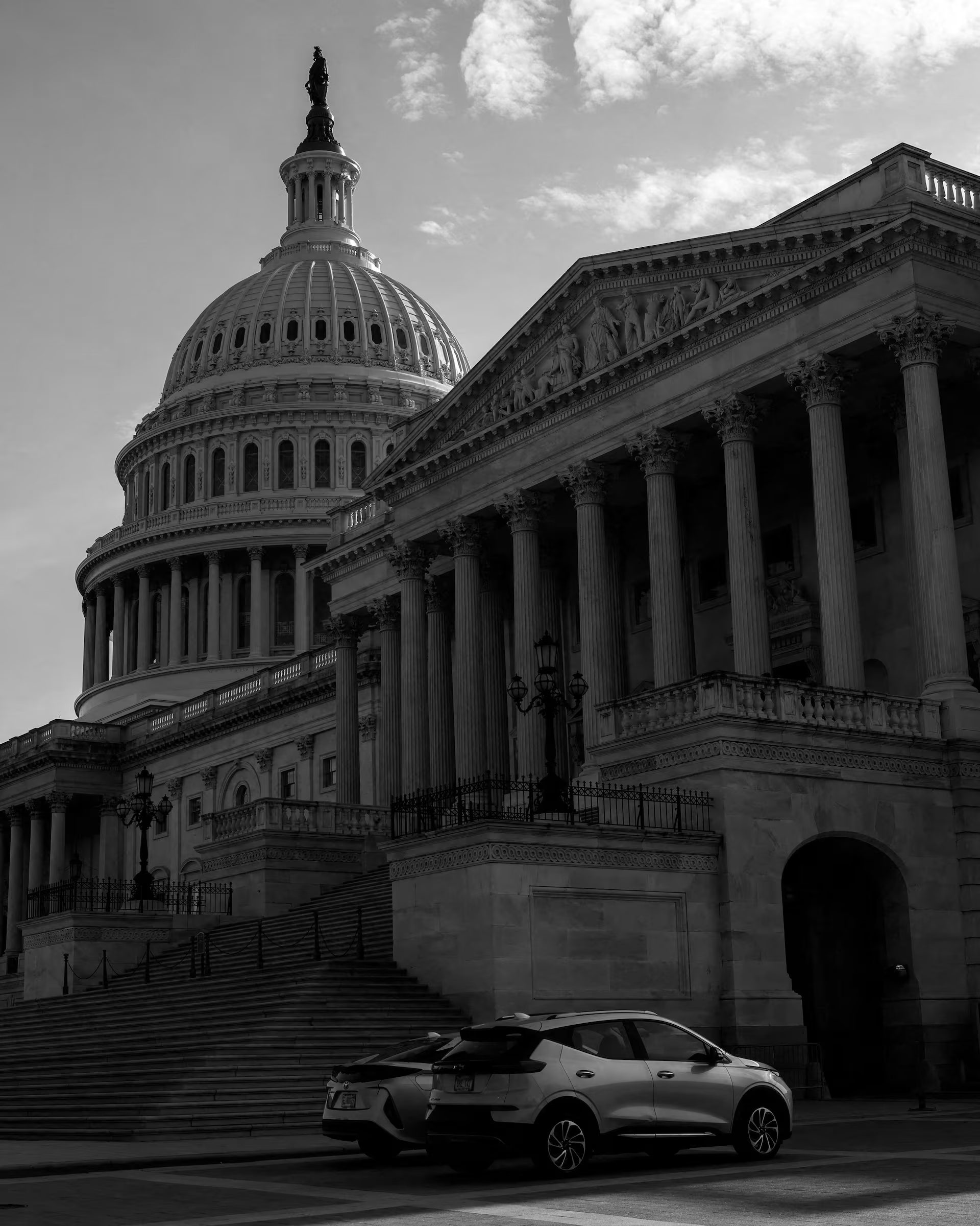 U.S. Capitol Building in black and white; cars parked in front of the steps.