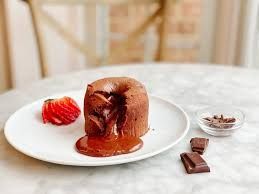 Chocoladelavacake met een vloeibare, gesmolten kern, aardbeien en stukjes chocolade op een bord.