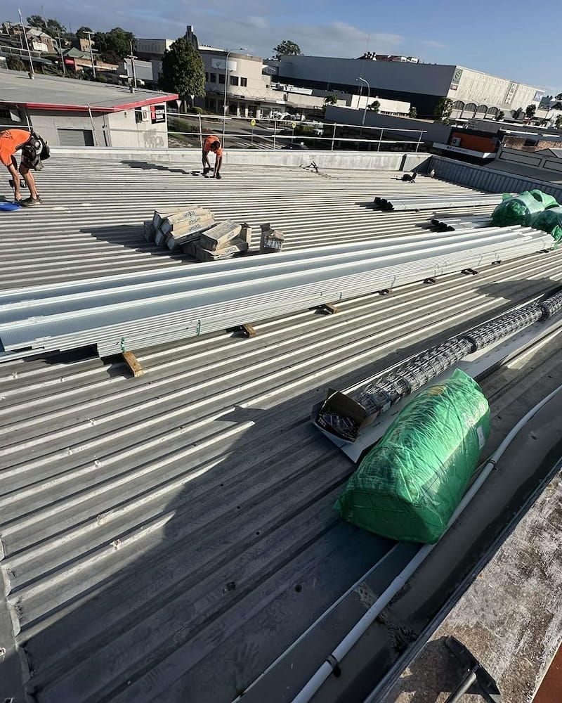 Workers on a Corrugated Metal Roof With Construction Materials — Ace1 Metal Roofing in Taree, NSW