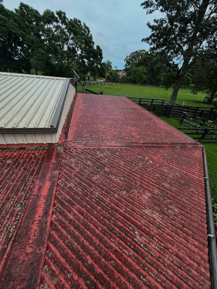 Red, Weathered Corrugated Metal Roof With a Building in a Grassy, Rural Setting — Ace1 Metal Roofing in Taree, NSW