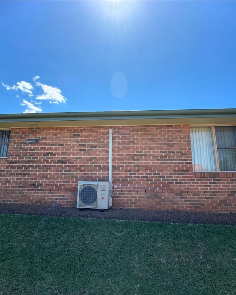 Air Conditioning Unit Against a Brick Wall, Below a Blue Sky — Ace1 Metal Roofing in Taree, NSW