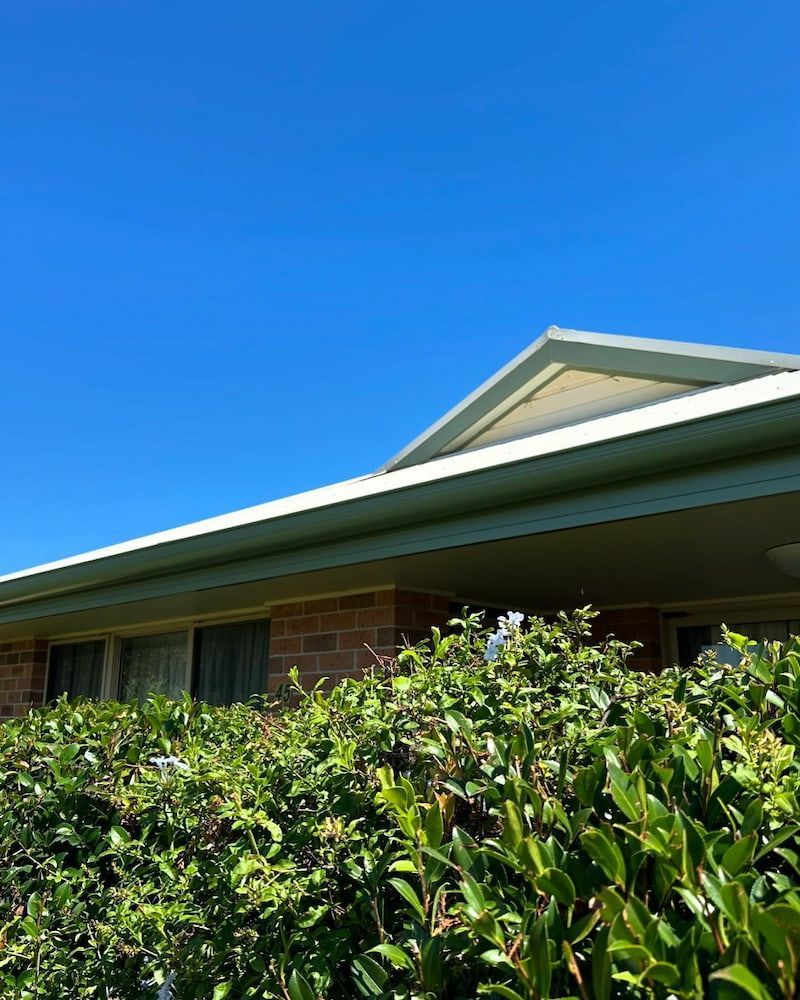 Brick Building With Green Hedge Beneath a Blue Sky — Ace1 Metal Roofing in Taree, NSW