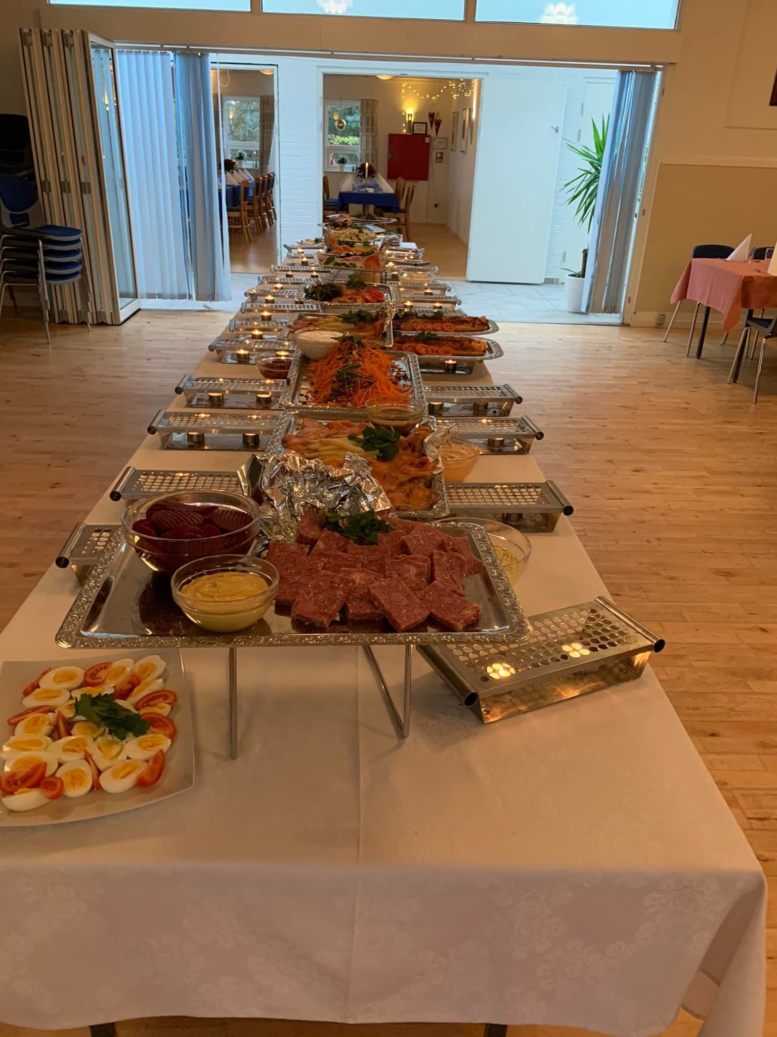 Langt buffetbord fyldt med mad i en klart oplyst eventsal.