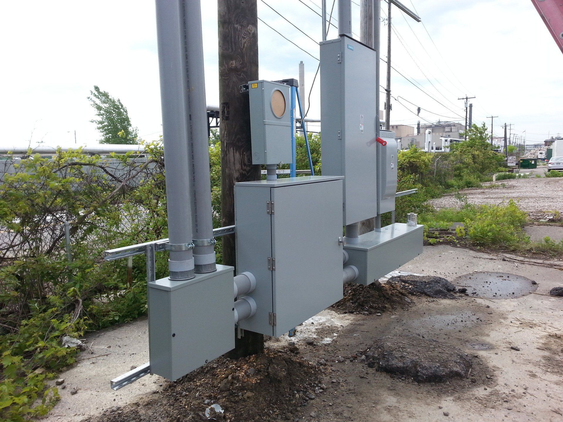 Gray electrical boxes and conduit mounted on a utility pole outdoors.