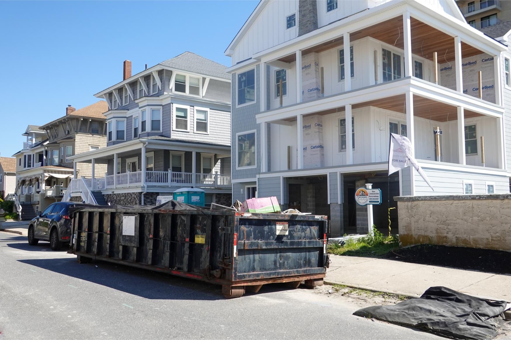 Street with large construction dumpster in front of white seaside houses under a blue sky