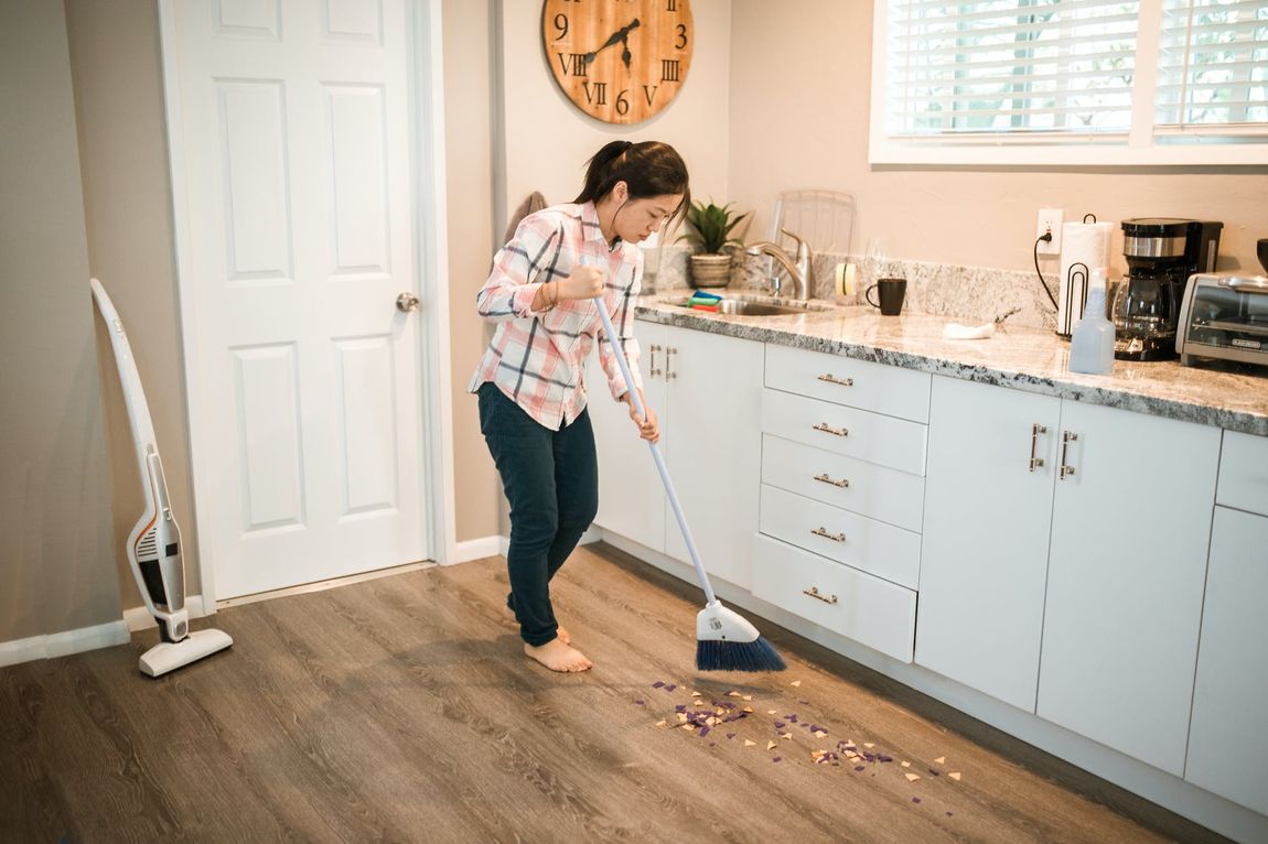 A woman is sweeping the floor in a kitchen with a broom.