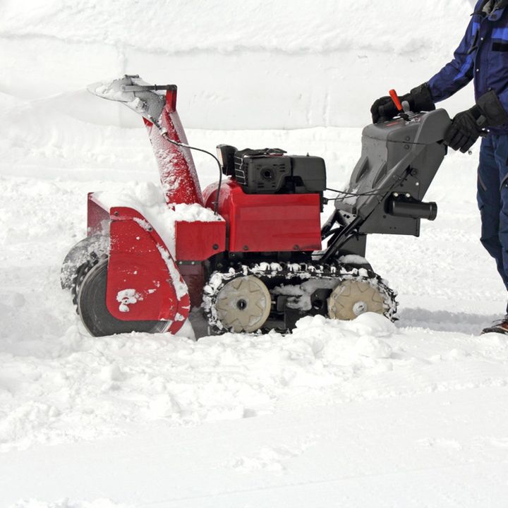 A man is pushing a red snow blower through the snow