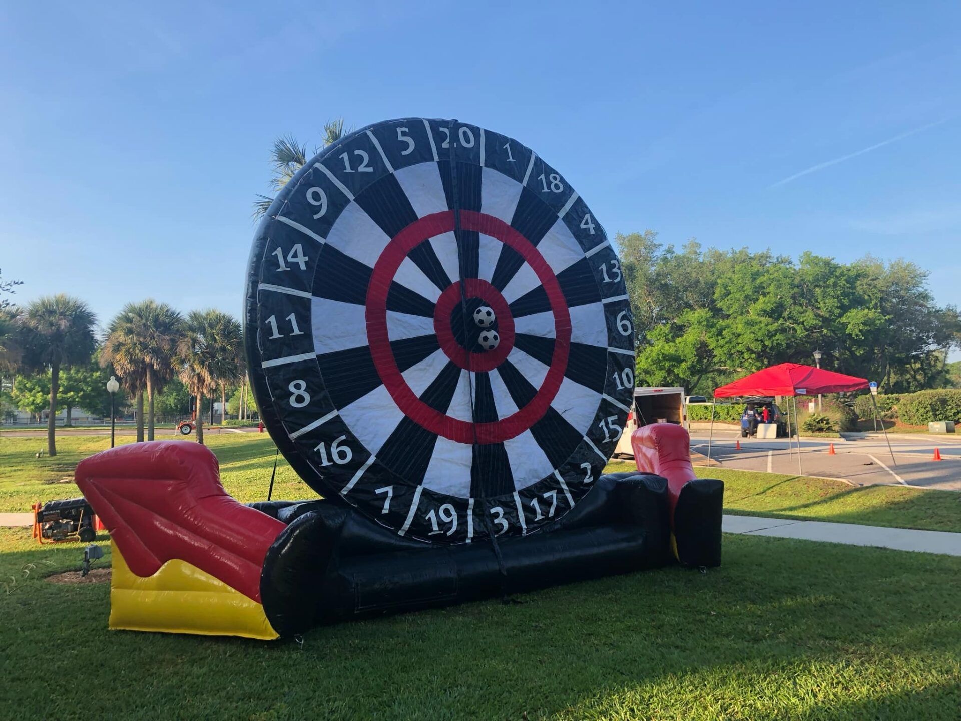 An inflatable dart board game set up on a grassy lawn under a clear blue sky.
