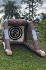 An inflatable axe-throwing game with a target board set up on a grassy lawn in front of a house.