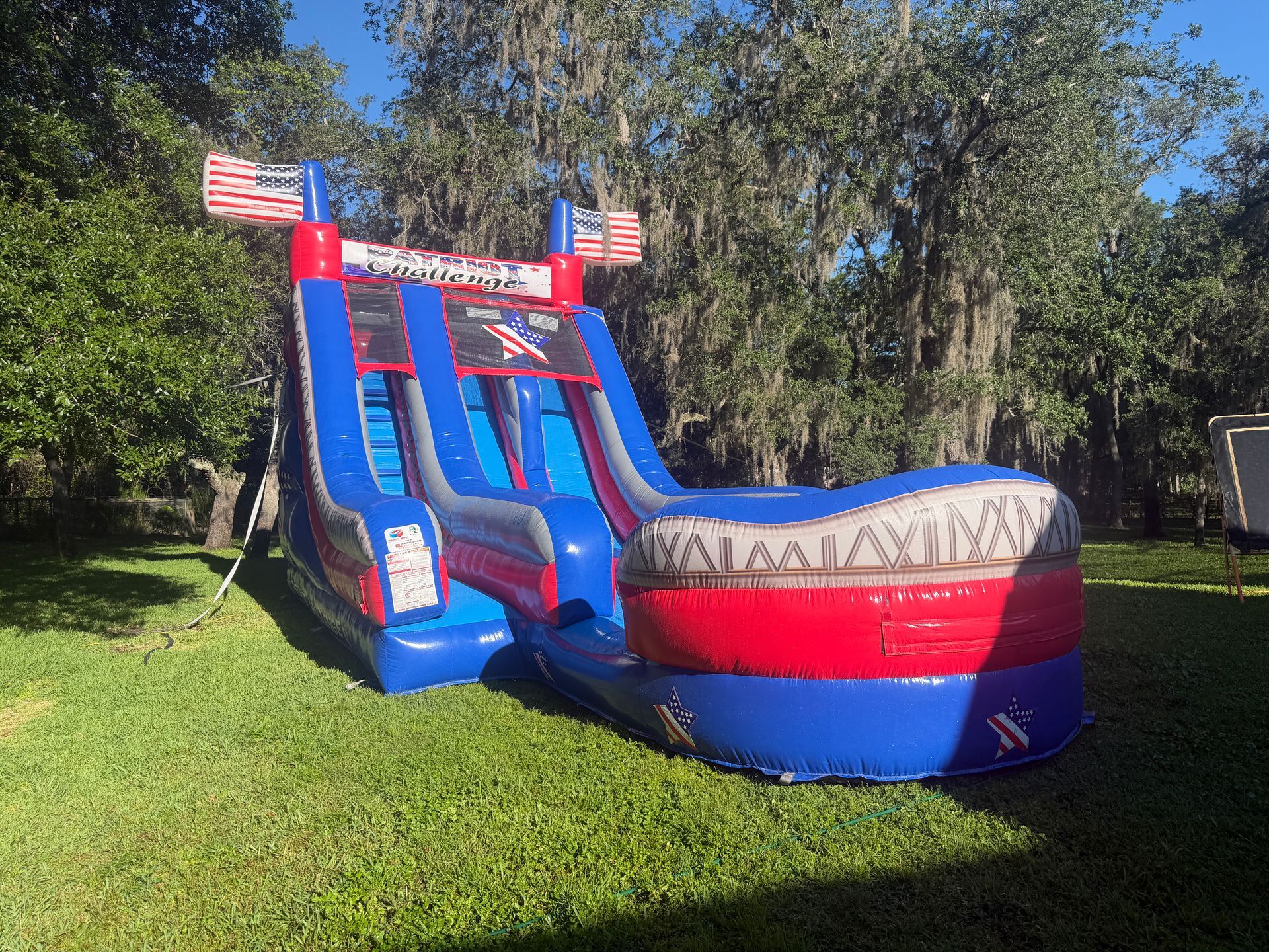 Red and blue inflatable water slide with American flags beside a large inflatable punching game on grass.