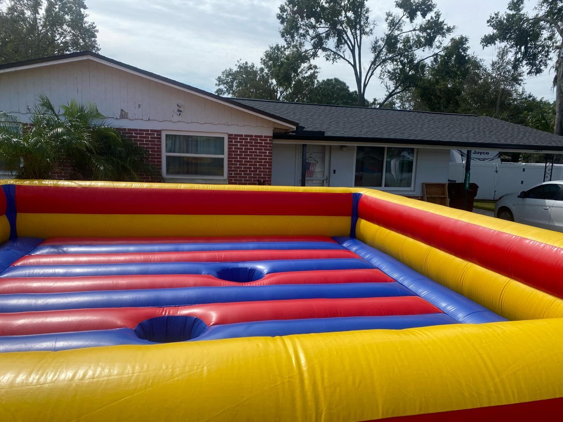 A large, inflatable red, yellow, and blue rectangular bounce house sits in front of a residential house.