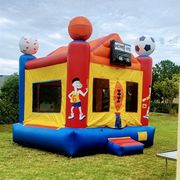 A sports-themed inflatable bounce house with basketball, baseball, and soccer ball accents, set on a green lawn.