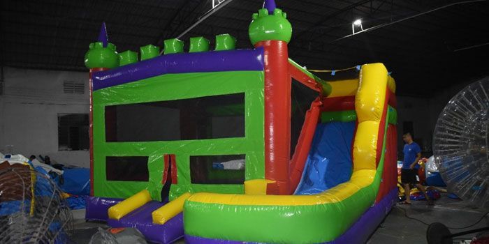 A colorful, multi-colored inflatable bounce house with an integrated slide, set up inside a warehouse-like building.