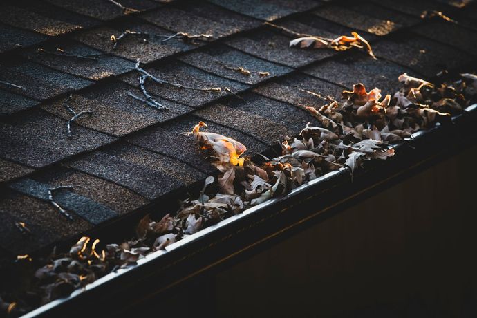 Close-up of a dark shingled roof with a gutter filled with dry leaves and a small flame