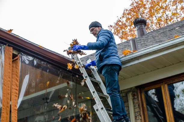 A man is standing on a ladder cleaning the gutters of a house.