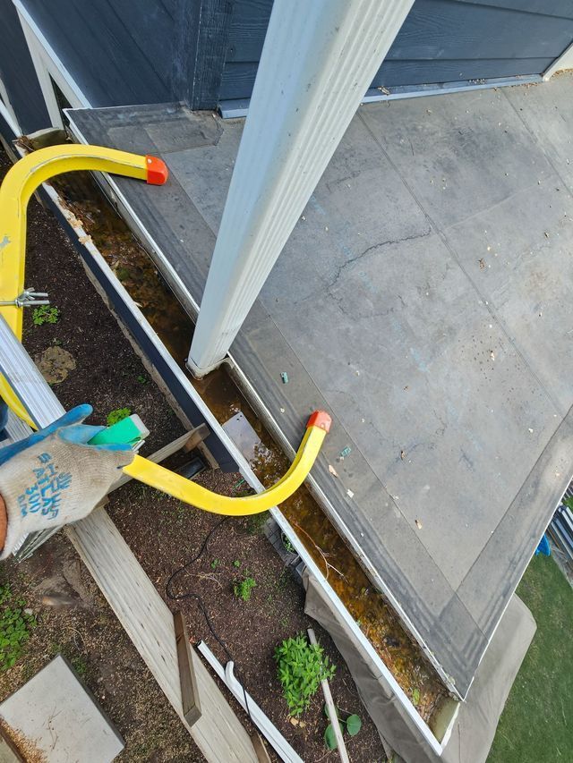 Gloved hand holding yellow railing on a porch beside white post and concrete steps
