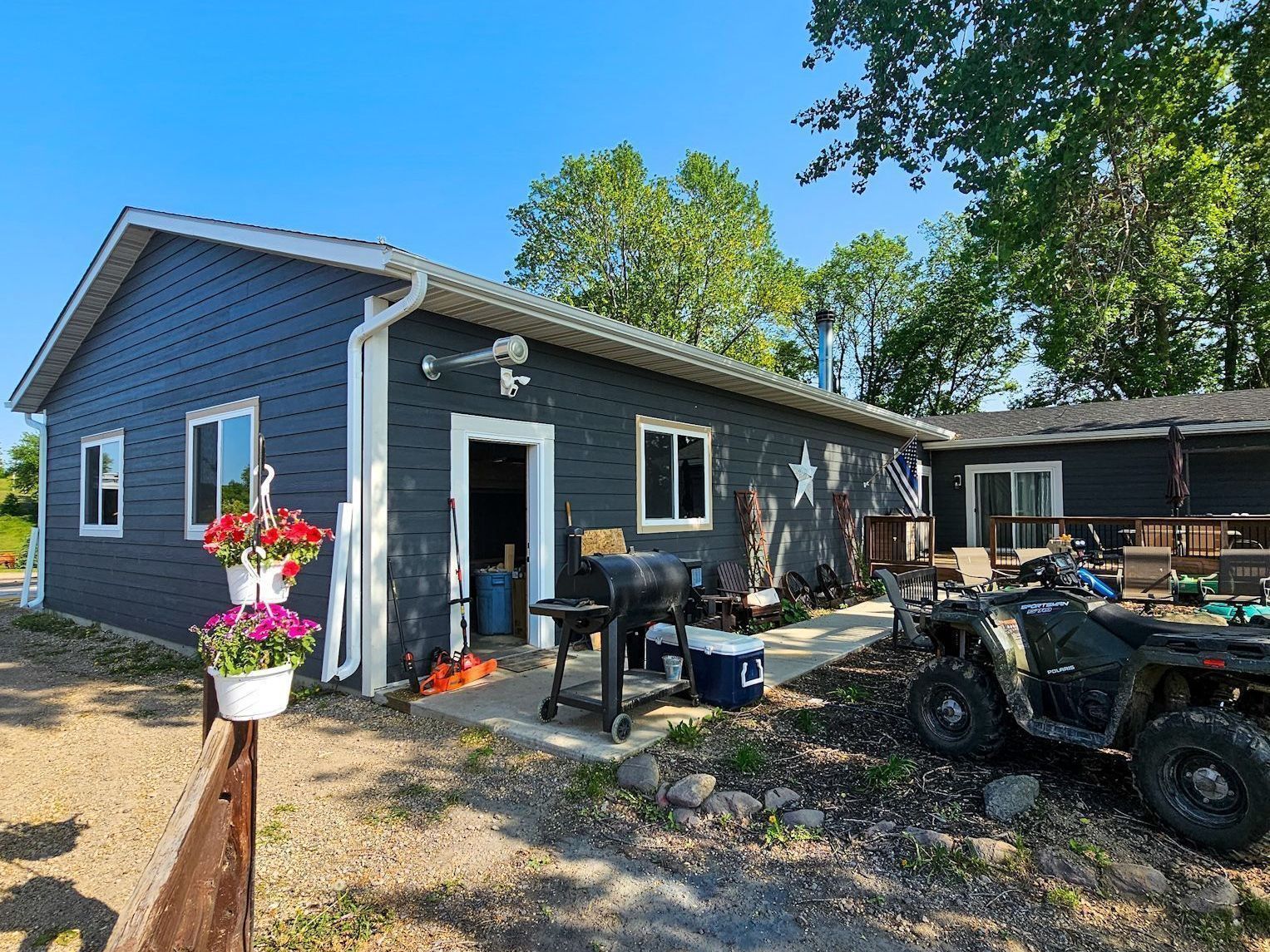 Dark gray house exterior with a porch, potted flowers, and an ATV parked on a gravel driveway.