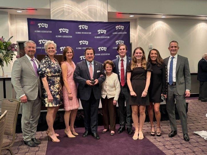A group of people are posing for a picture in front of a tcu banner.