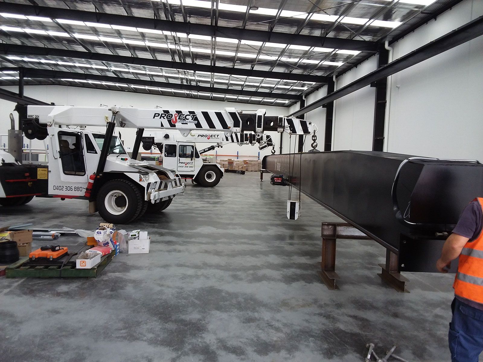 A man in an orange vest is working on a piece of equipment in a warehouse.