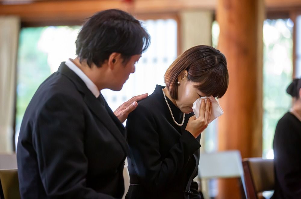 Woman crying, comforted by another at a funeral.