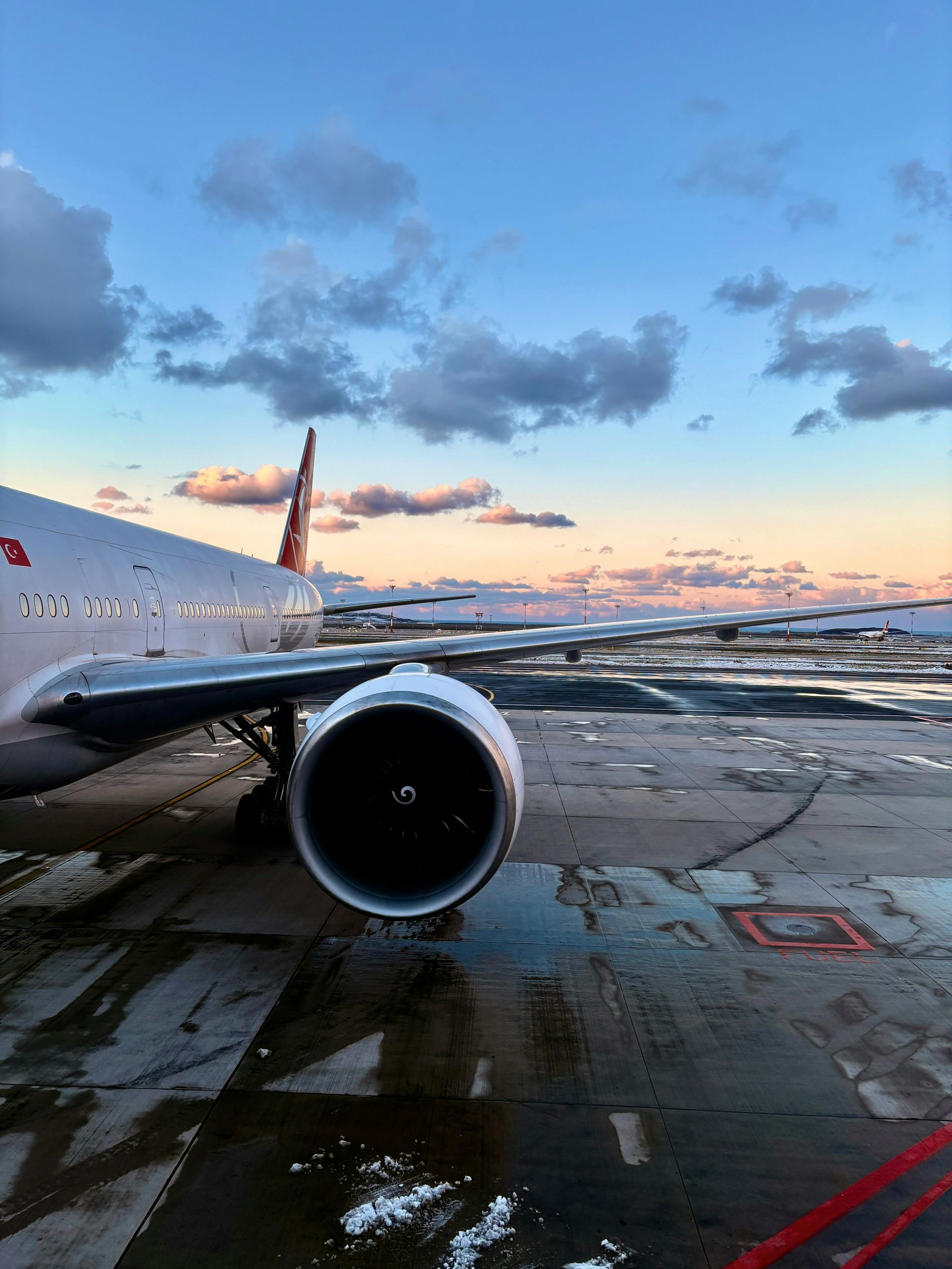 Airplane wing and engine on a wet tarmac; cloudy sky at dusk.