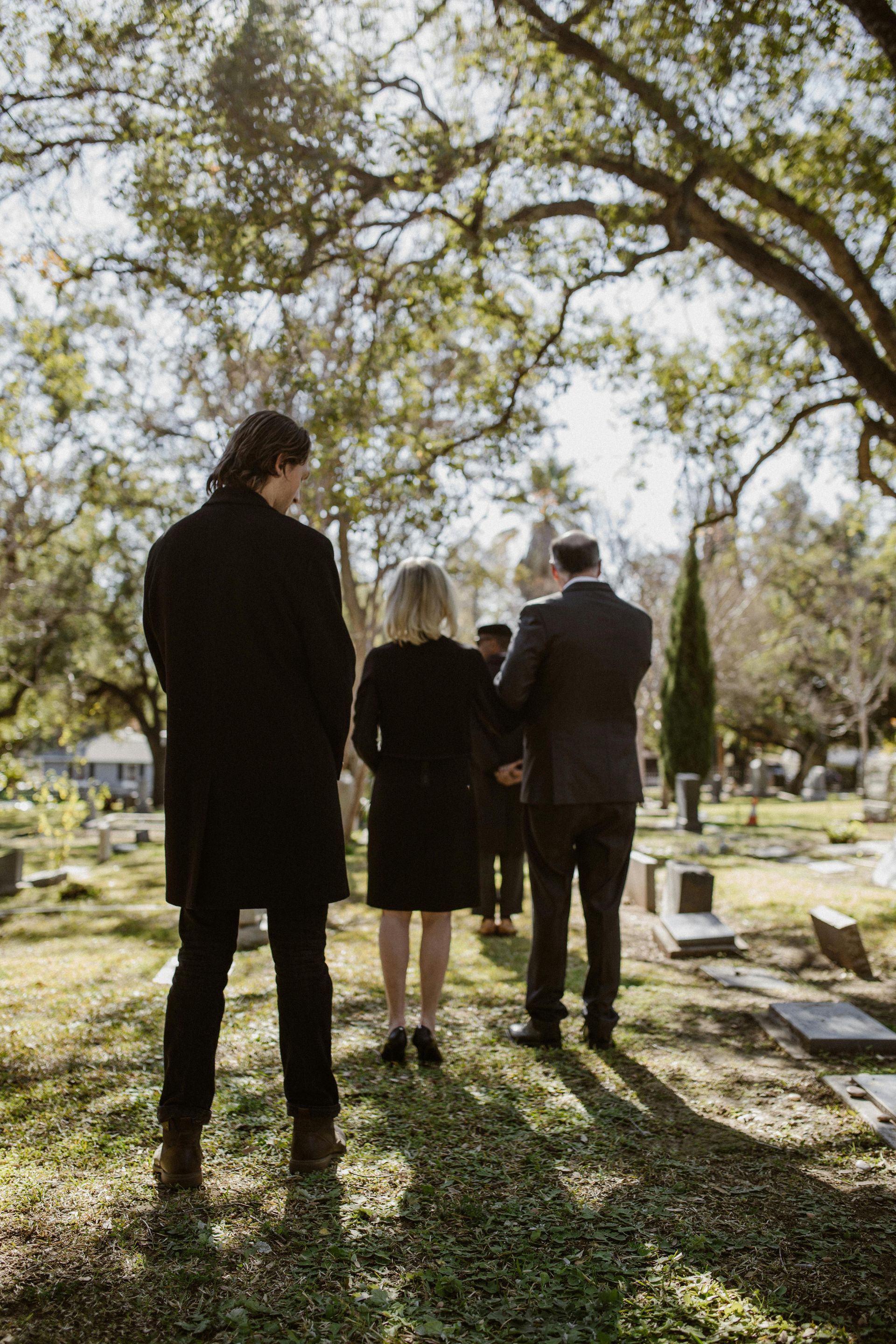 People at a graveside service in a cemetery. Trees overhead.