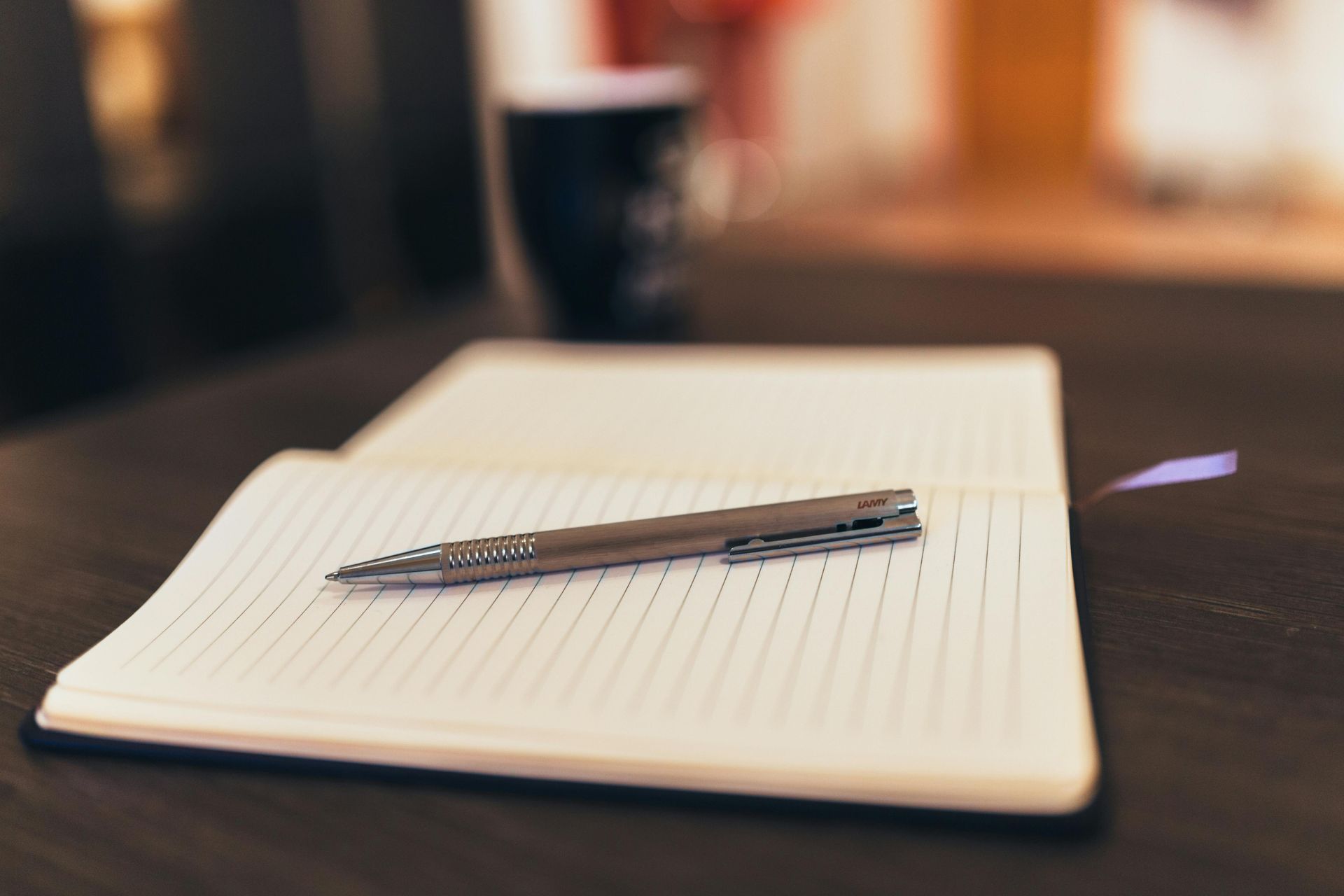 Notebook open with pen on top; a coffee cup in soft focus behind.