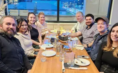 Group of nine people smiling around a table at a restaurant, with plates, glasses, and food.