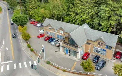A two-story building with cars parked in front, next to a road with a crosswalk and trees.