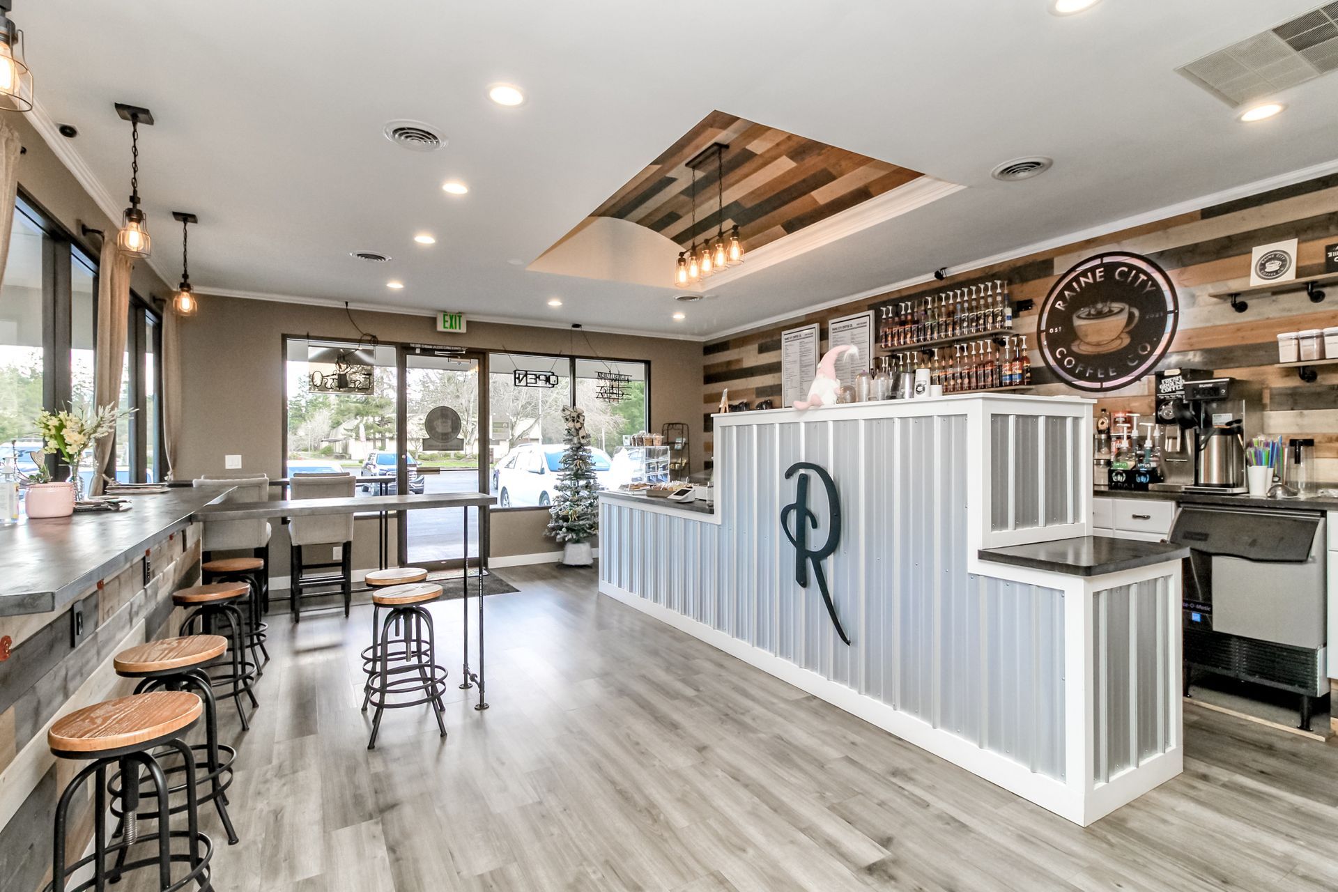 Coffee shop interior with bar, tables, and stools; wood and metal accents.