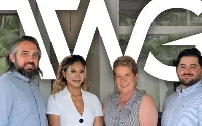 Four people standing in front of a building with TWG logo: a man with a beard, a woman, a woman with short hair, and a man.