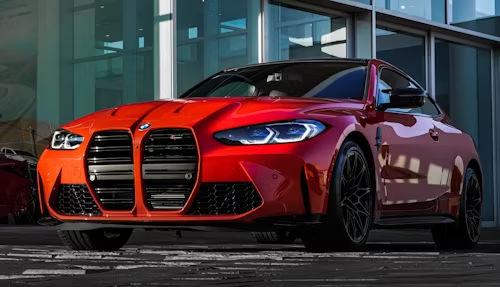 Red BMW sedan parked outside a modern glass building at dusk