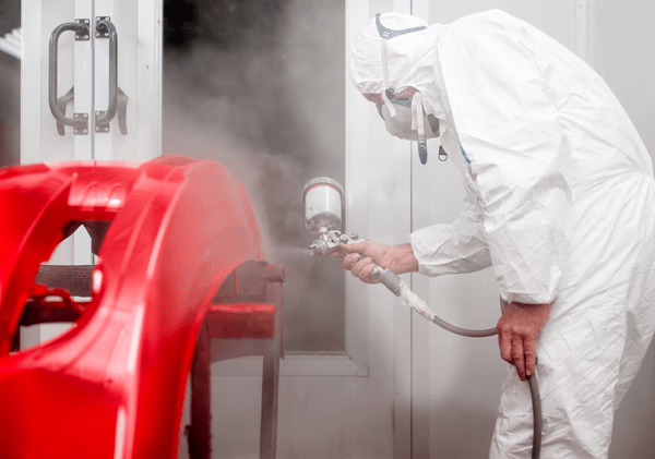 A man in a white suit is spray painting a red car.