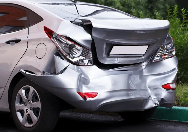 A silver car with significant rear-end damage, featuring a crushed bumper and trunk, parked outdoors.