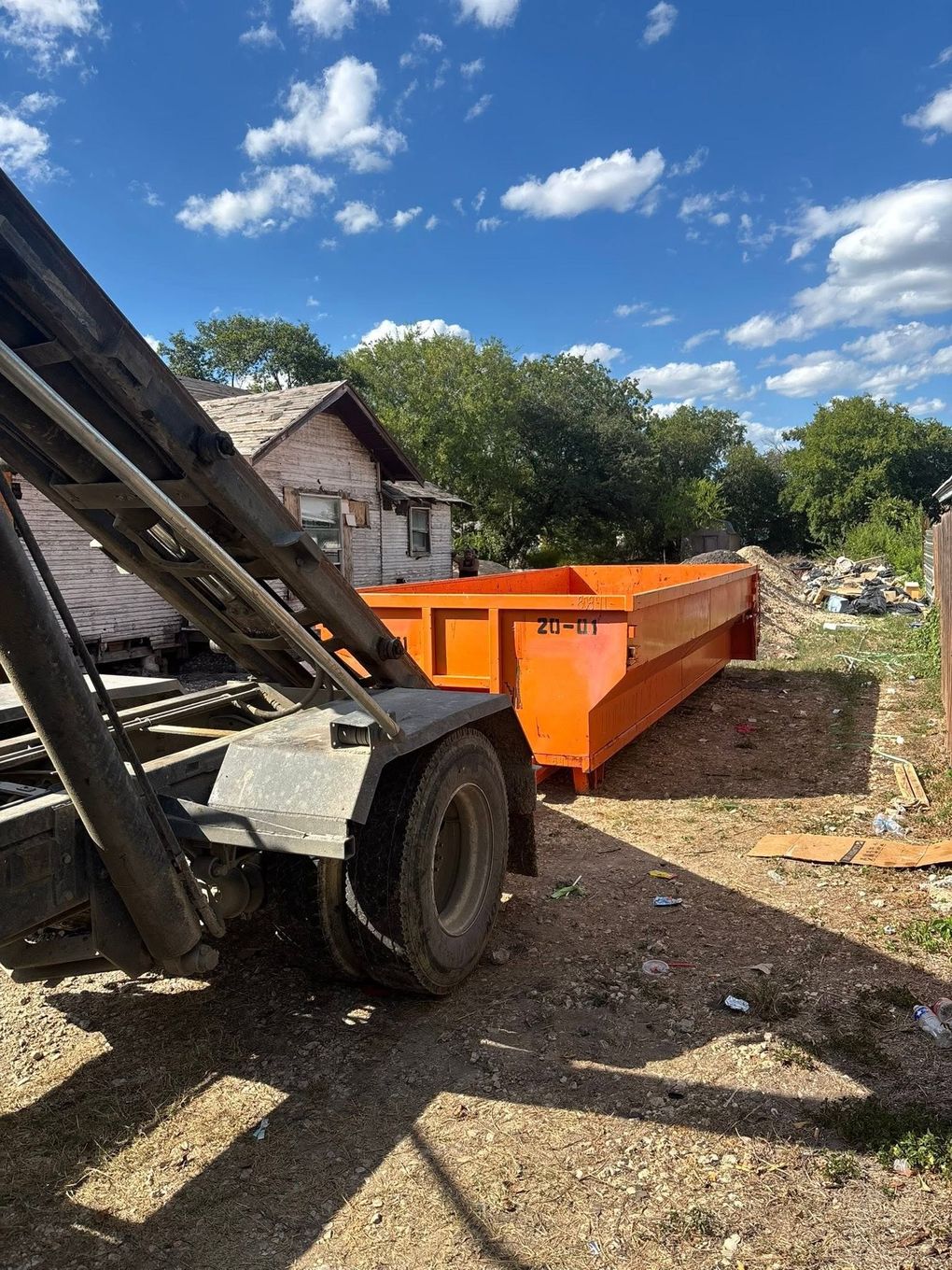 Orange dump trailer hitched to a tractor in a gravel yard under a blue sky.