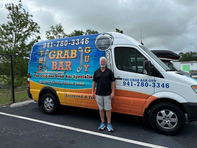 Person standing in front of a blue-and-orange Grab Bar moving van in a parking lot