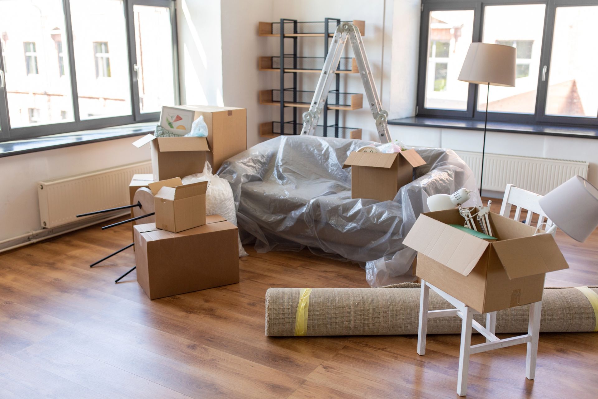 Cajas y muebles en una habitación, listos para mudanza. Cajas de cartón, alfombra enrollada y sofá forrado.