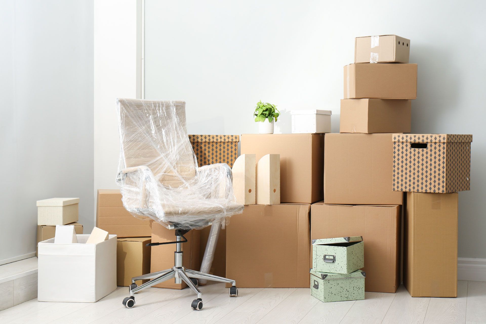 Silla de oficina envuelta en plástico junto a cajas de mudanza apiladas en una habitación blanca.